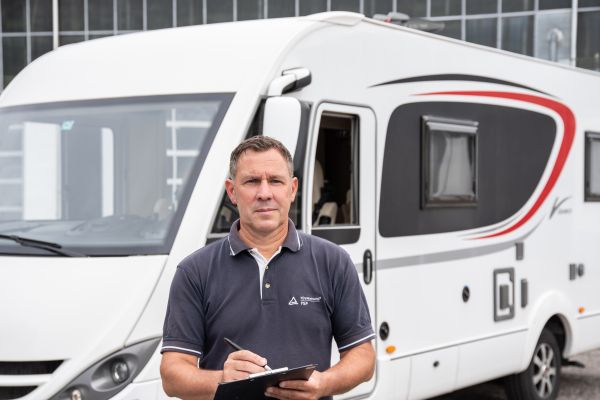 FSP-Sachverständige Jan Baumstark prüft einen Caravan mit Klemmbrett vor einem Gebäude, sorgt für Sicherheit und Verkehrstüchtigkeit