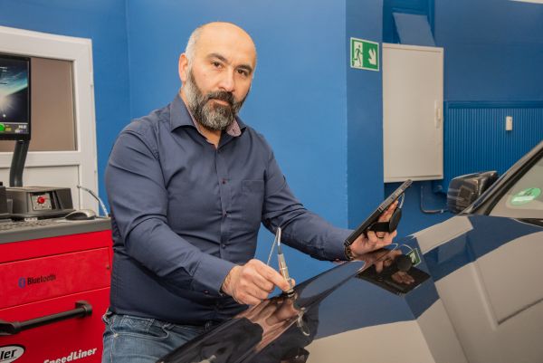 Baris Altin, Kfz-Prüfingenieur der FSP, prüft mit Tablet und Messgerät ein Fahrzeug in einer modernen FSP Prüfstelle